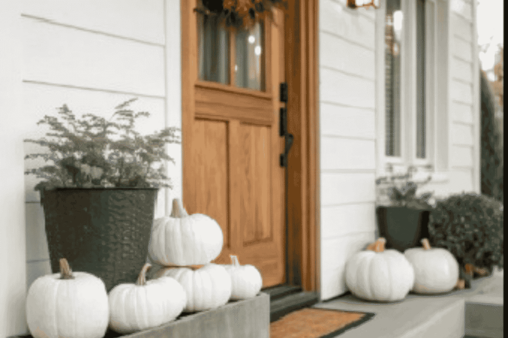 Neutral fall front porch decorated with white pumpkins and seasonal greenery